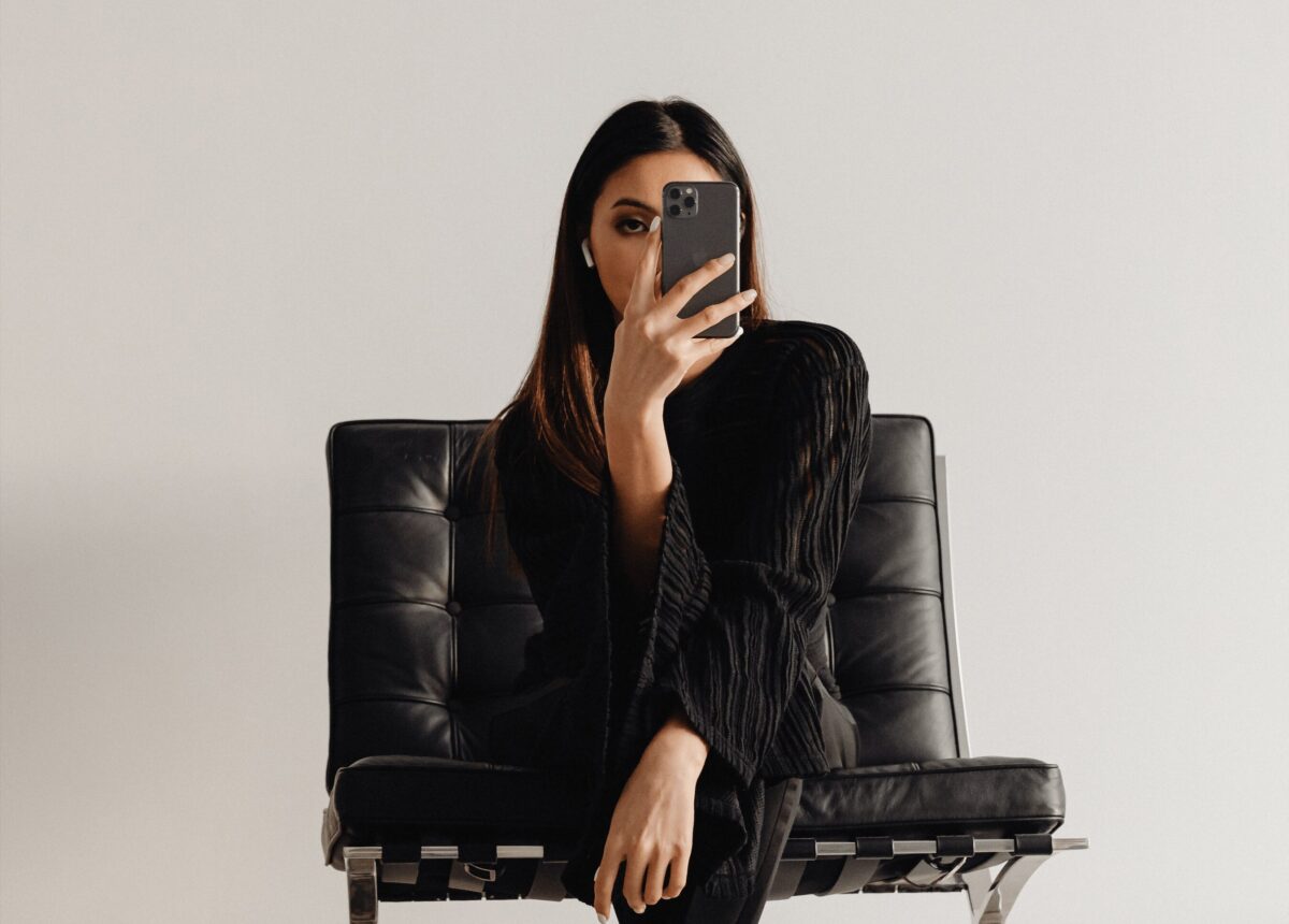 Femme habillée en noir, assise sur un fauteuil en cuir, fixant son téléphone. Une image illustrant les conséquences de la dépendance au téléphone.