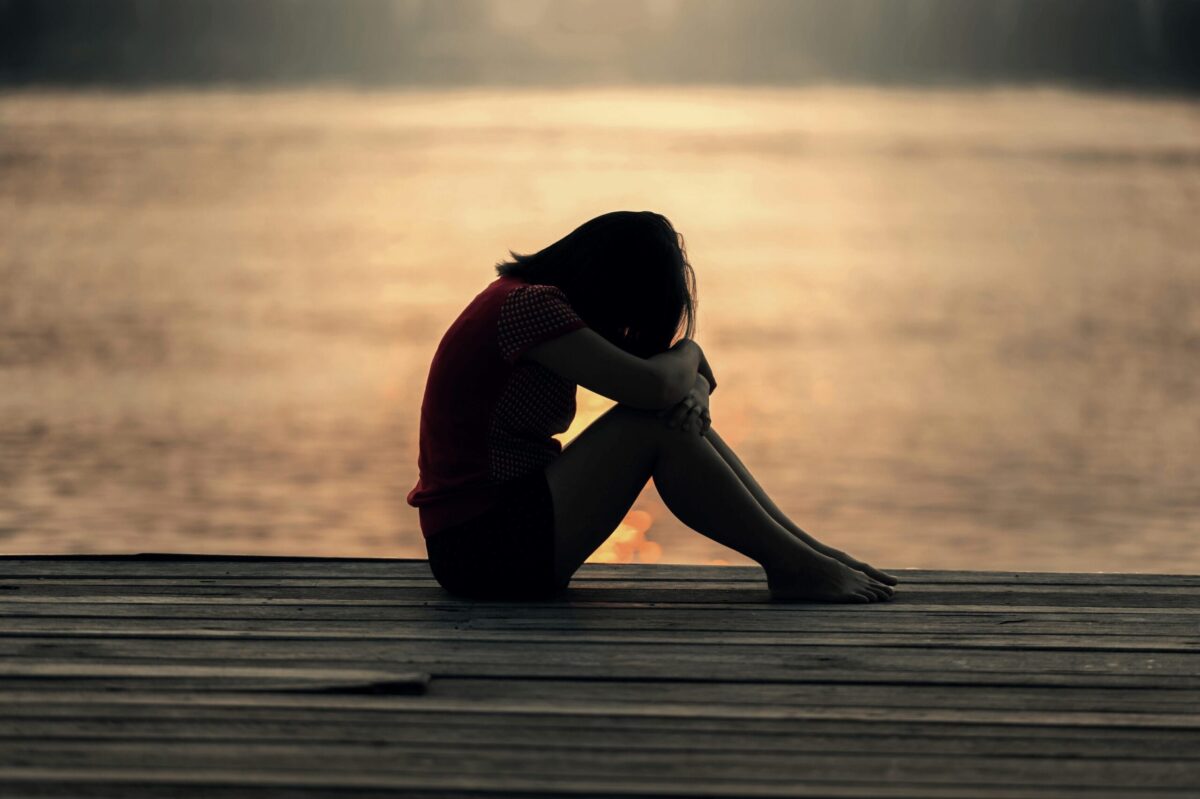 Femme assise seule au bord de l'eau, perdue dans ses pensées, illustrant le concept de rumination et son impact sur la santé mentale.