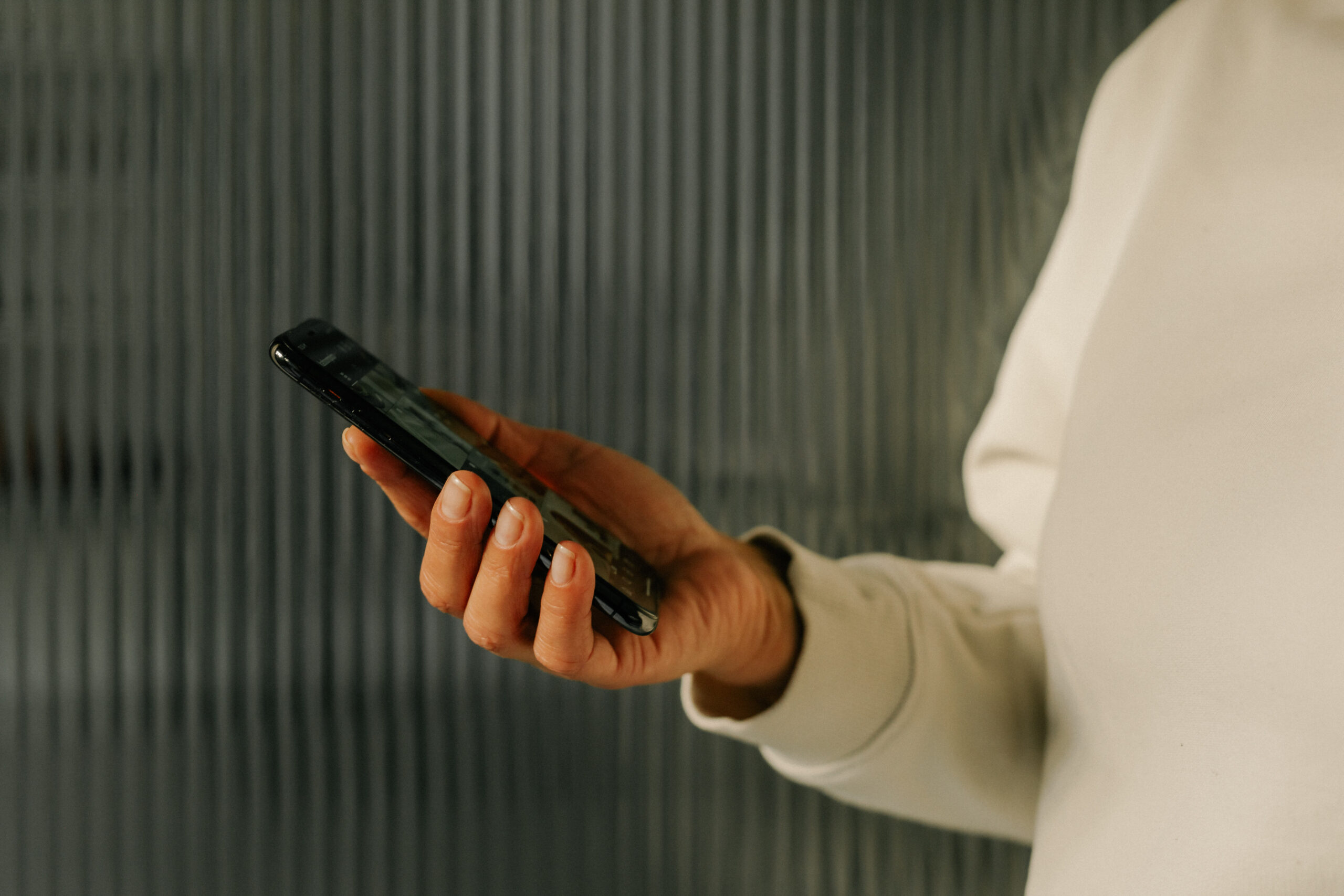 Gros plan sur une main tenant un smartphone. La posture suggère que la personne lit ou s’apprête à interagir avec l’écran. L’image illustre une scène quotidienne liée à la technologie et aux réseaux sociaux."