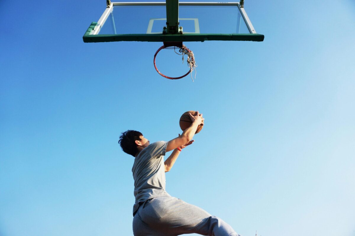 Un joueur de basketball en plein saut s’apprête à réaliser un dunk sur un panier extérieur. L’image capture un moment d’effort physique et de passion sportive, source de ressource pour contrer le burnout. 